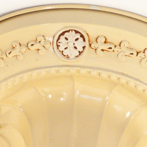 this picture shows the floral detail on the canopy of a vintage bare bulb ceiling fixture. The floral detail in this picture is butter yellow